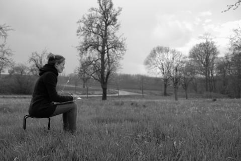 Eine Frau sitzt auf einem Stuhl auf einer Wiese und zeichnet.